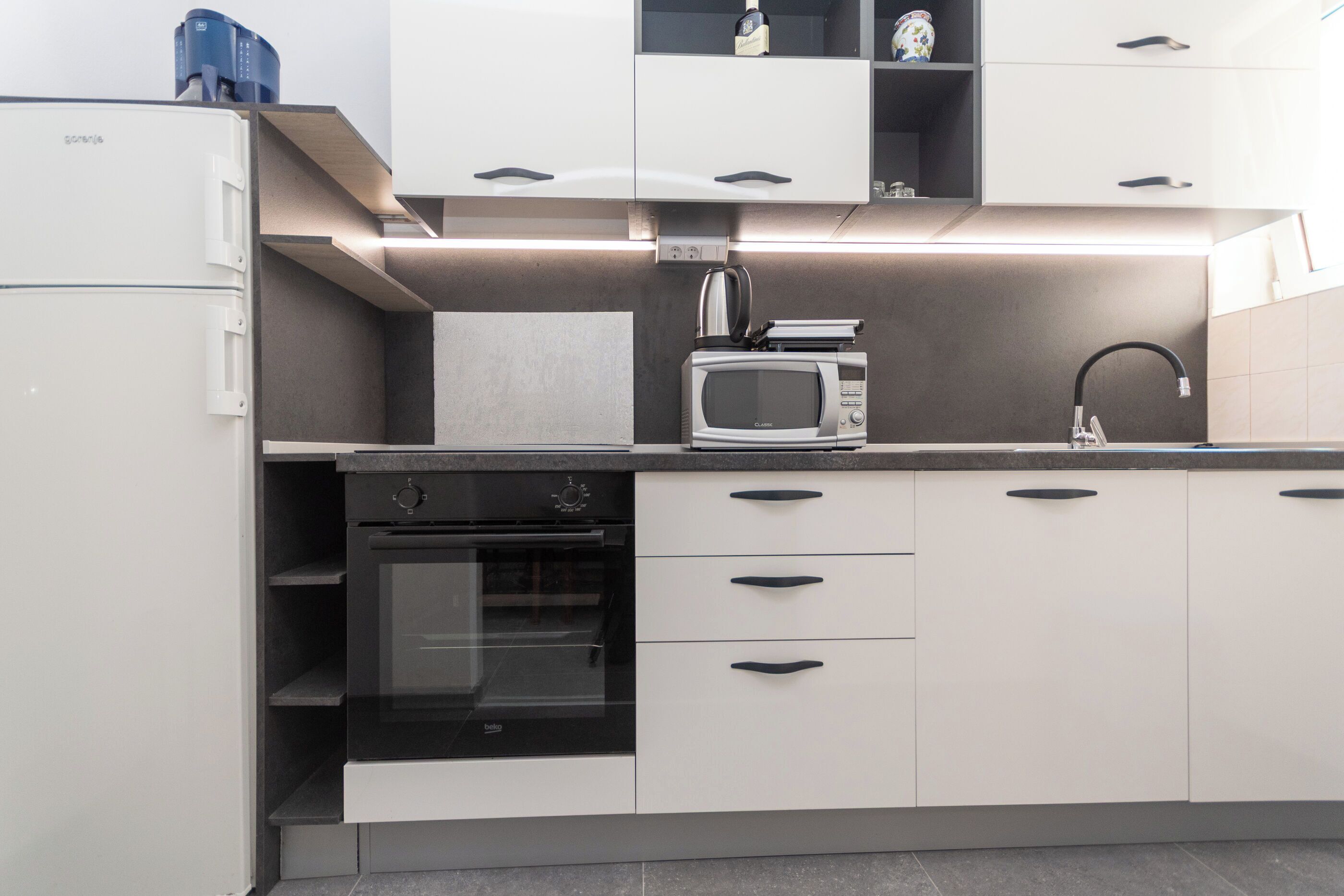 A modern kitchen with a built-in oven, microwave, and a coffee machine.