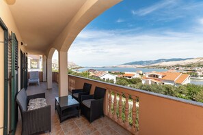 Ein Balkon mit Gartenmöbeln, Blick auf eine Küstenstadt und eine gebirgige Landschaft.