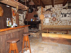 Ein rustikaler Innenraum mit einer Steinwand, einer Holztheke, Hockern und einer Bank.