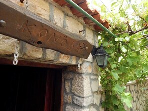 Ein Steinhaus mit einem rustikalen Holzschild, auf dem 'KONSEH' steht, und einem schwarzen Laternenaufsatz daneben.