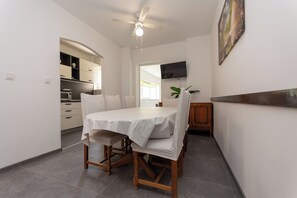 Ein Essbereich mit Tisch, Stühlen, einem Deckenventilator, einem Fernseher und einer Küche im Hintergrund.