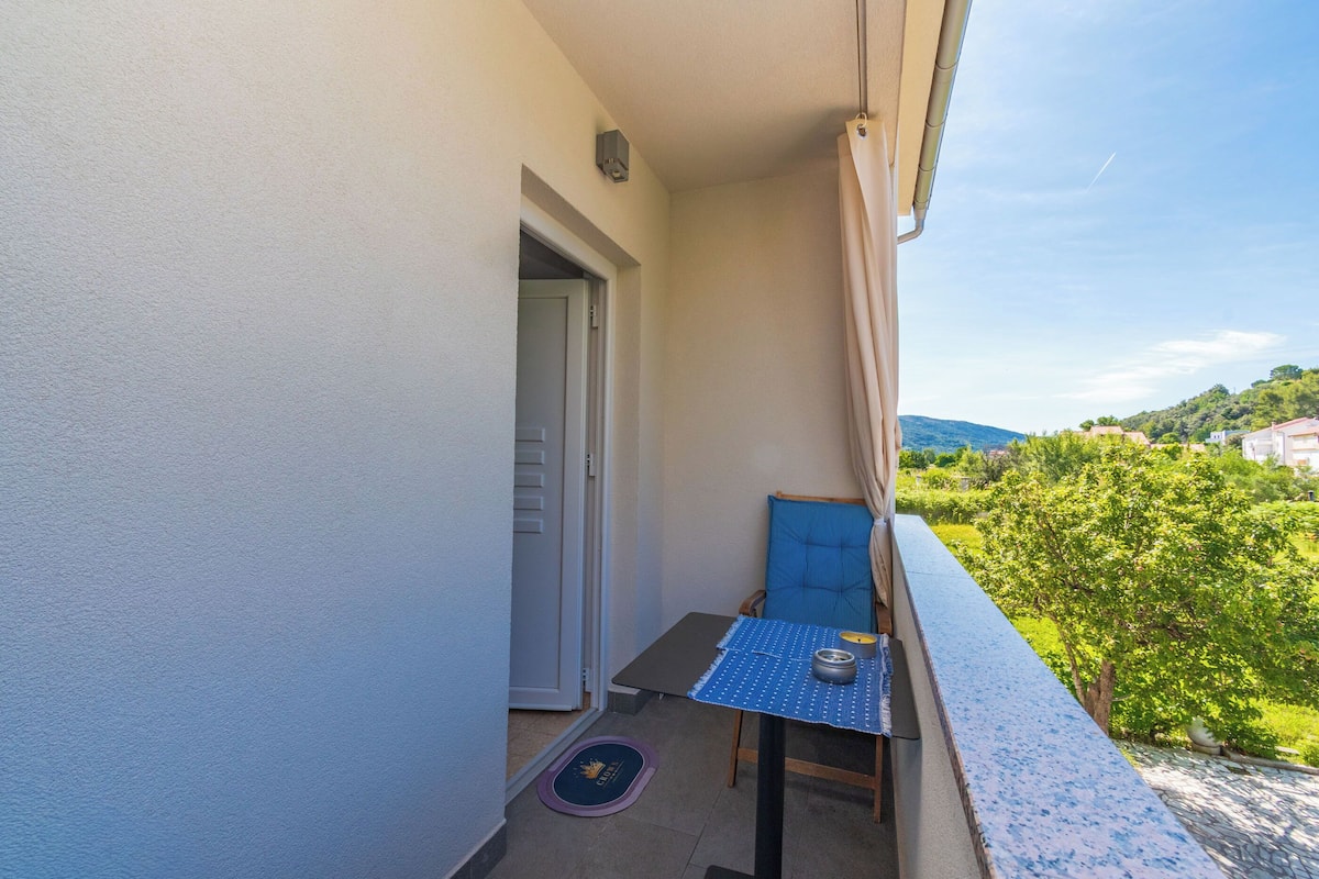 A balcony with a small table, a chair, and a view of greenery and hills.