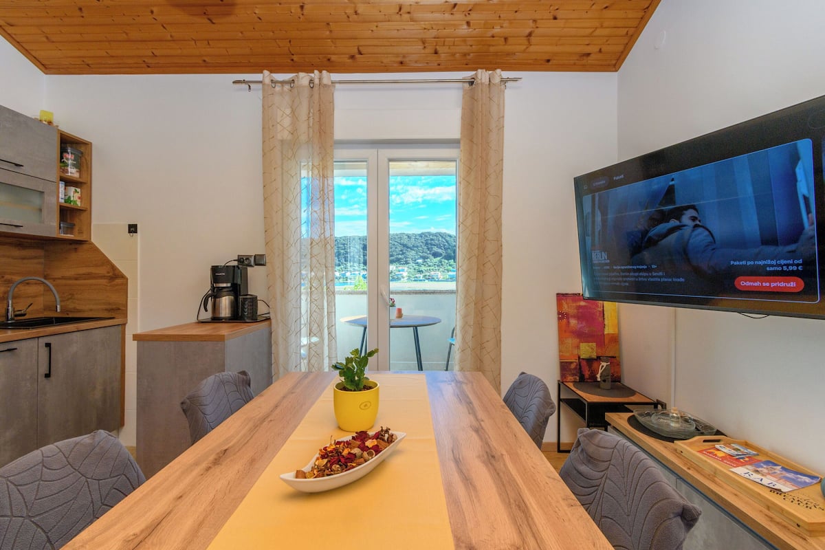 A modern kitchen with a wooden ceiling, a dining table with a yellow placemat, and a TV mounted on the wall.