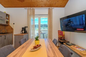 A modern kitchen with a wooden ceiling, a dining table with a yellow placemat, and a TV mounted on the wall. - Apartments Angela (Rab)
