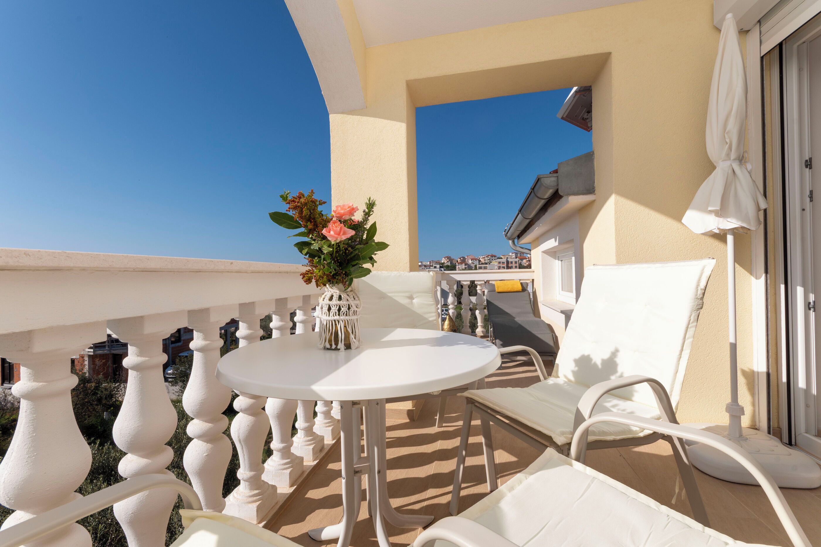 Un balcon avec une table blanche, des chaises blanches et un vase à fleurs.