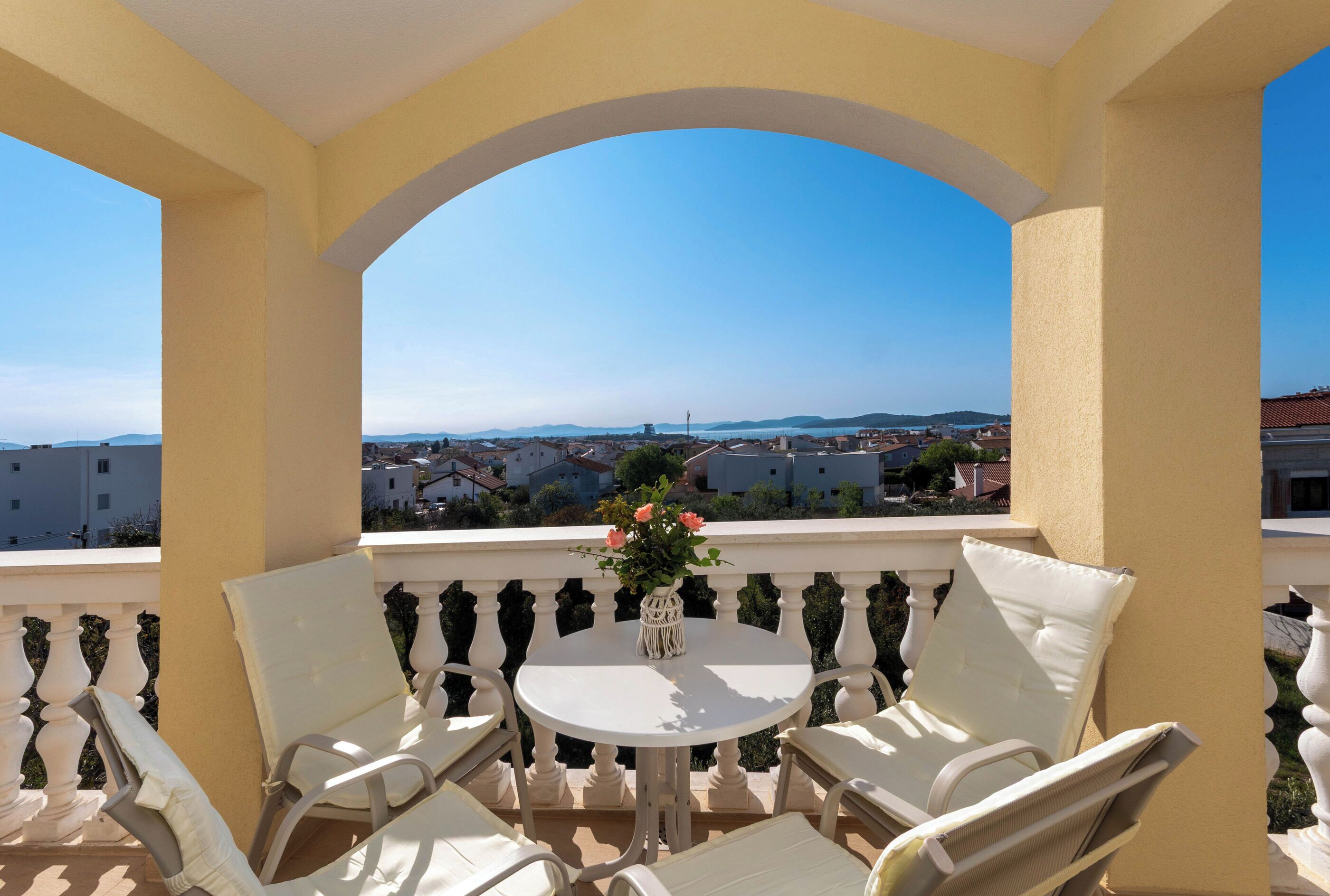 Un balcon avec des chaises blanches, une table ronde et un vase de fleurs.