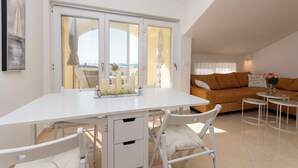 A modern living room with a white dining table, white chairs, a brown sofa, and a balcony with a view. - Apartments VV Adriatic Panorama (Vodice)