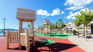 A playground with slides and climbing structures, benches, and a red and green play area. - Apartments VV Adriatic Panorama (Vodice)