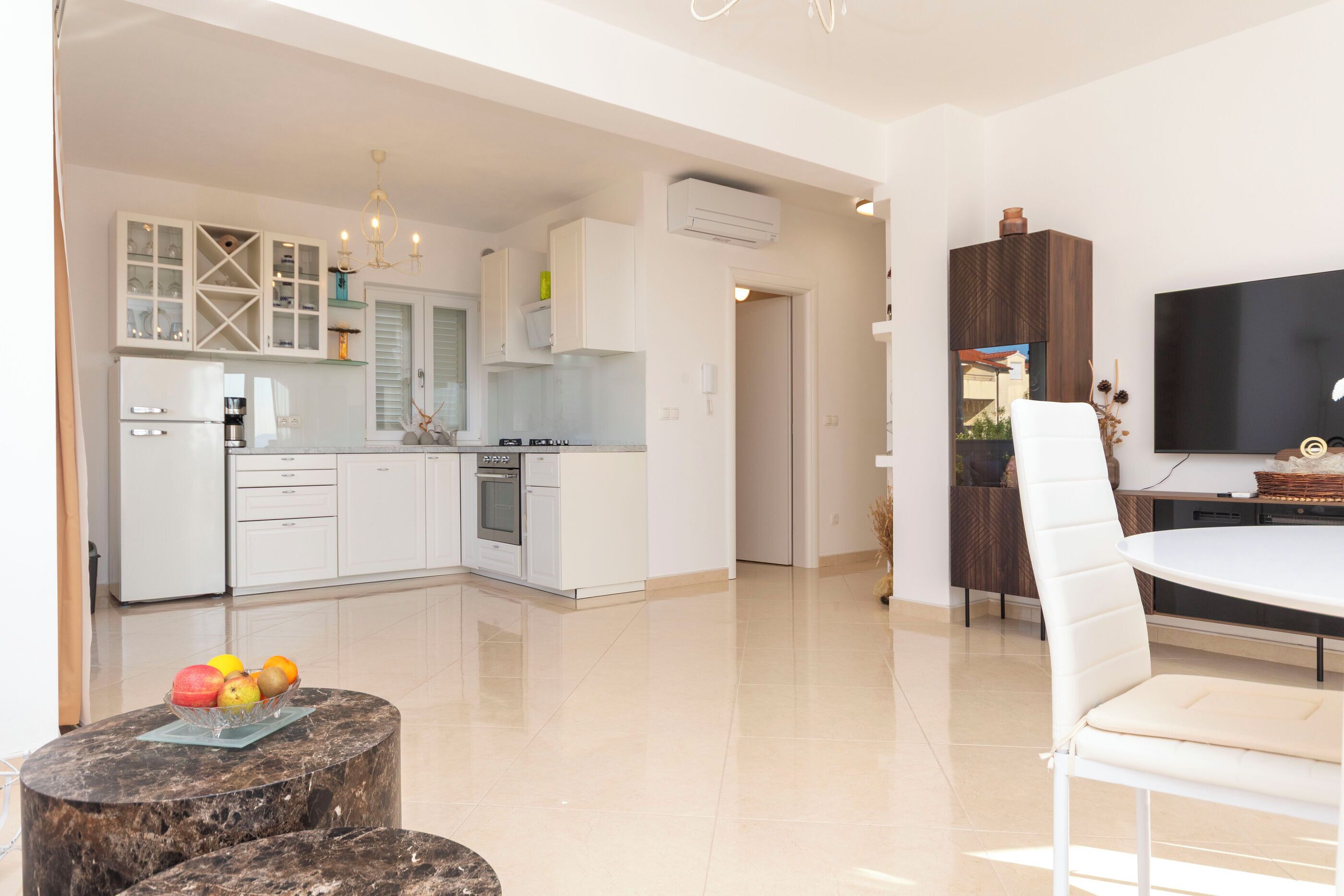Une cuisine moderne avec des meubles blancs, un coin repas comprenant une table et des chaises blanches, et un téléviseur à écran plat fixé au mur.