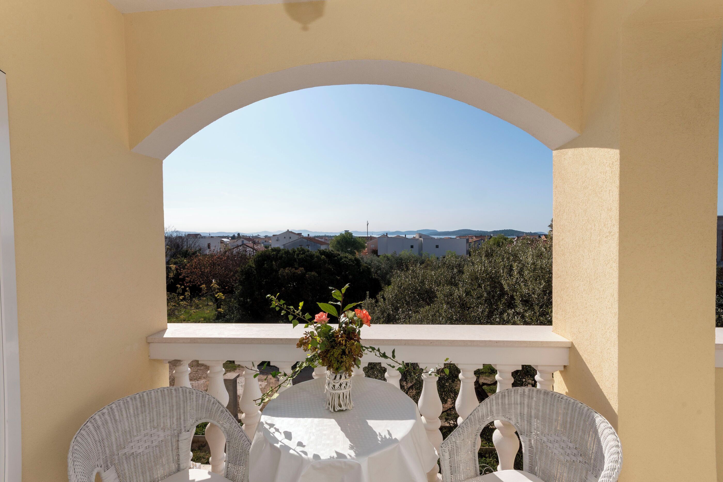 A balcony with a table and chairs, a vase with flowers, and a view of the landscape.
