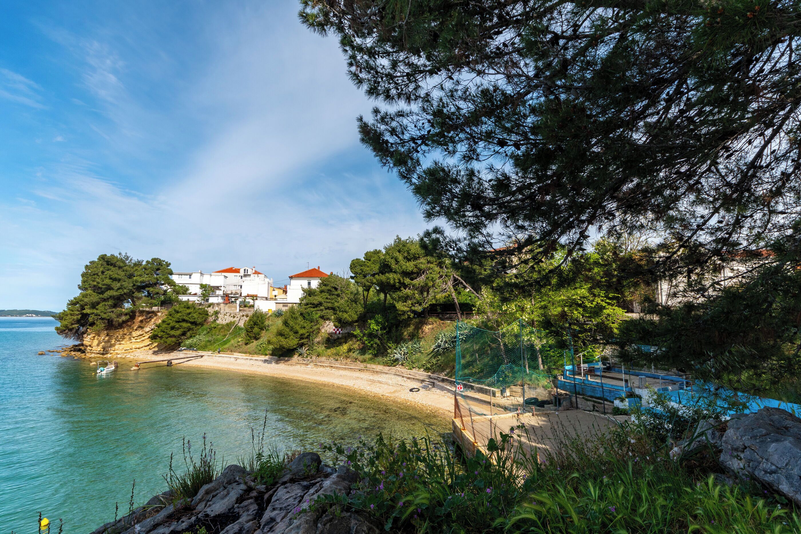 A coastal scene with a beach, clear water, and buildings on a cliff.