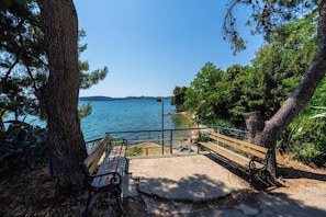 Eine Bank mit Blick auf einen Strand, mit freiem Blick auf das Meer und ferne Hügel.