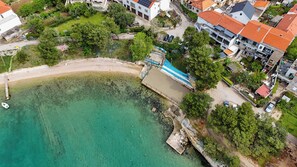 Ein Luftbild einer Küstenregion mit Strand, Steg und Wohnhäusern mit roten Ziegeldächern.