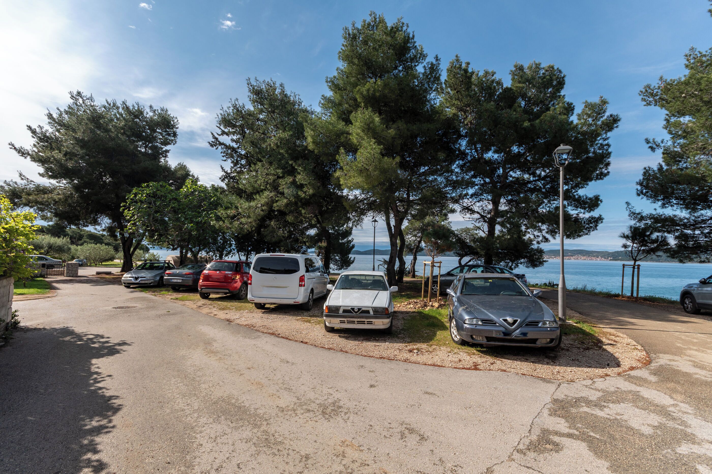 Un parking avec des voitures, des arbres et une vue sur la mer.