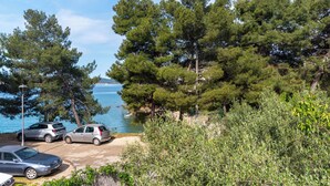 Ett kustnära område med parkerade bilar, täta, grönskande träd och fri utsikt över havet.