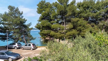 Uma área costeira com carros estacionados, árvores verdes densas e uma vista clara do mar.