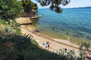 A beach with clear water, a rocky outcrop, and people swimming. - Apartment Kalma (Zadar)