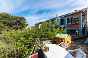 Eine Terrasse mit Tisch und Stühlen, ein kleines Spielhaus und ein Gebäude mit Balkonen.