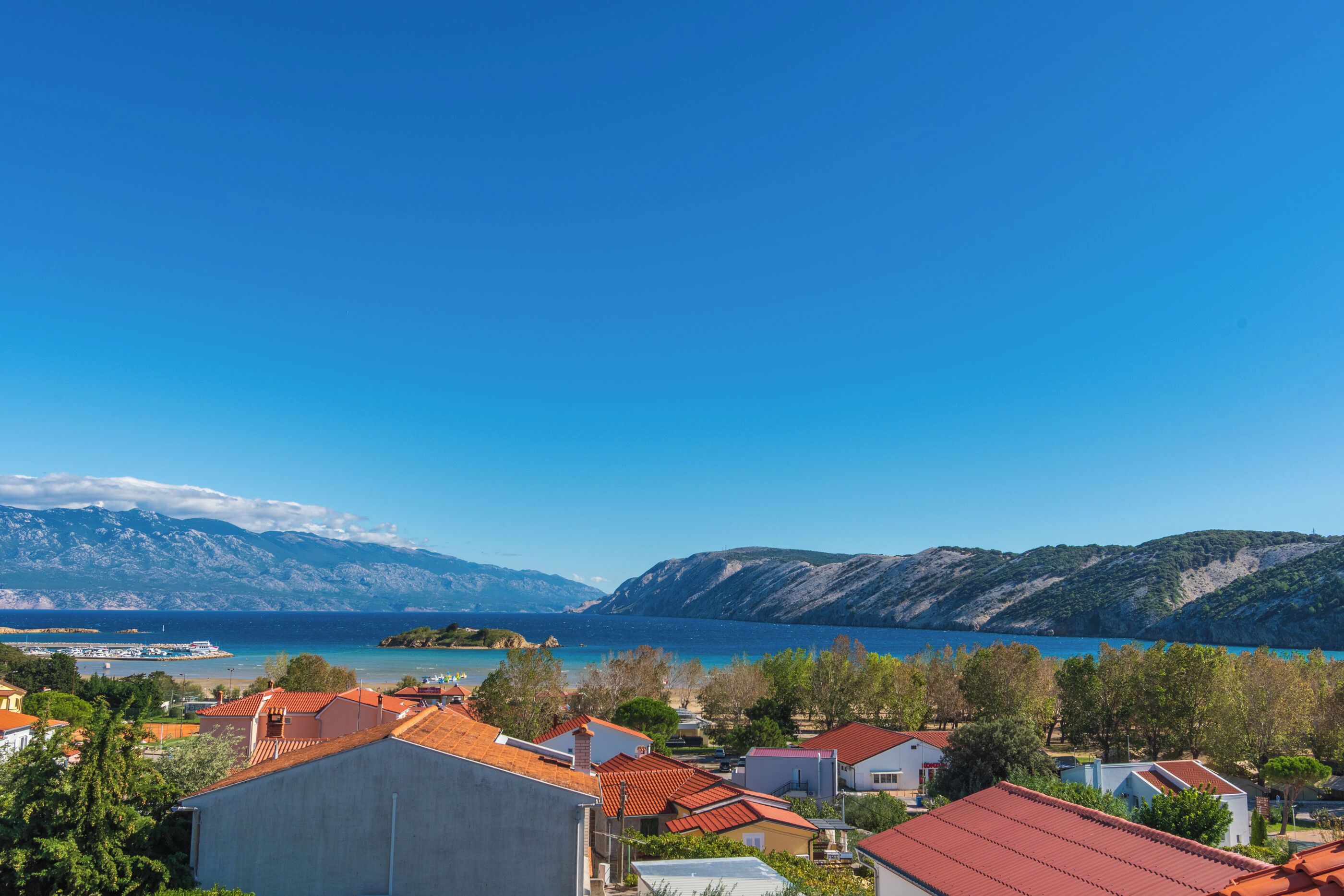 A coastal town with houses, a clear blue sky, and mountains in the background.