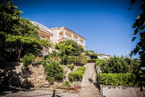 Ein mehrgeschossiges Gebäude mit einer Sandsteinfassade, einem Balkon und einer Treppe, die zum Eingang führt.