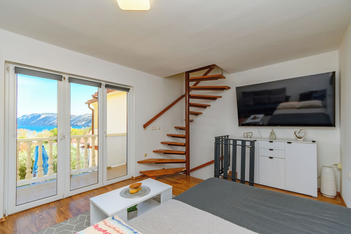 Ein modernes Wohnzimmer mit einer Holztreppe, einem Flachbildfernseher und einem Balkon mit Blick auf die Berge.
