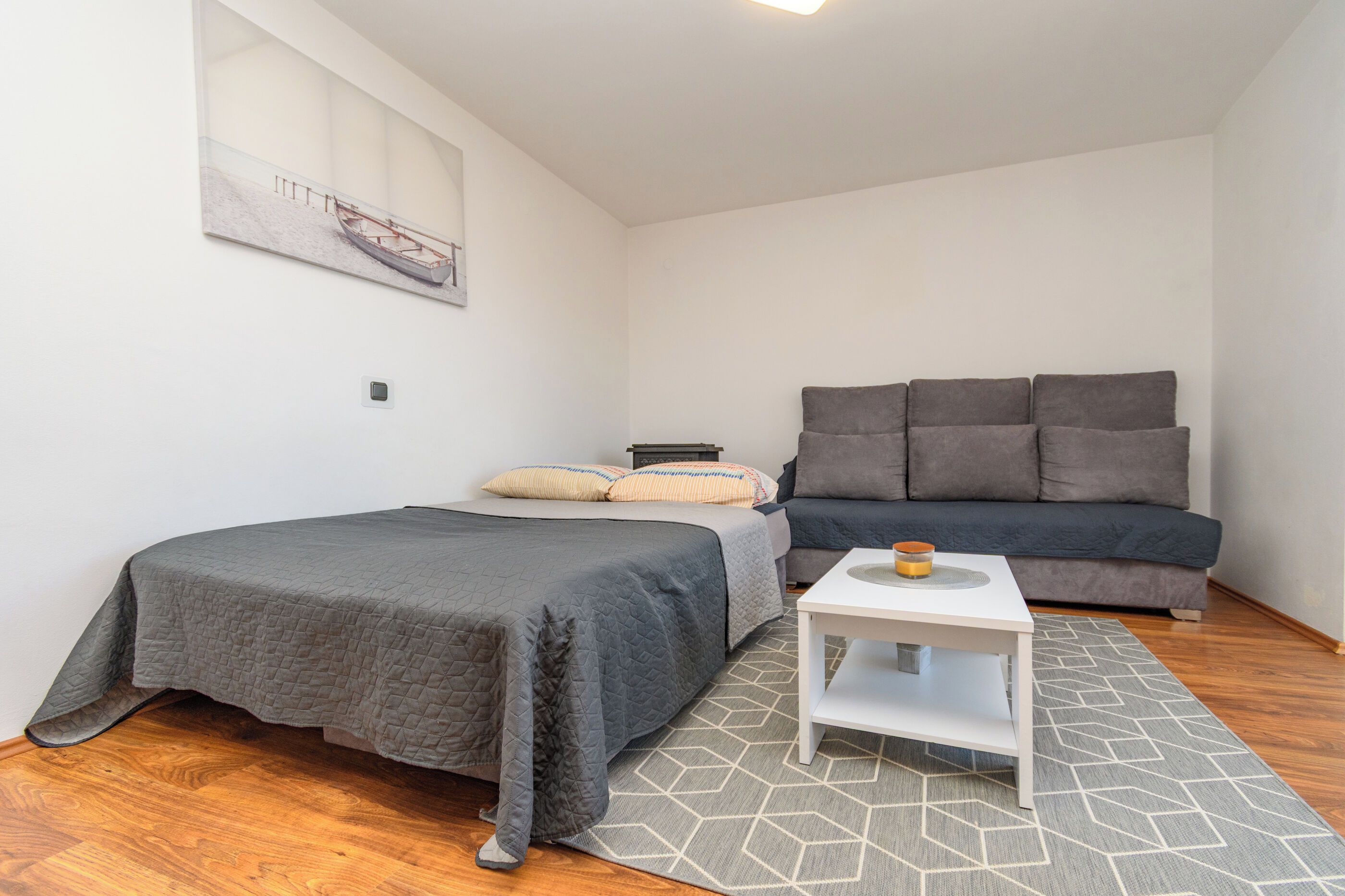 Un dormitorio compacto con cama, sofá, una mesita y un tapete estampado geométricamente.