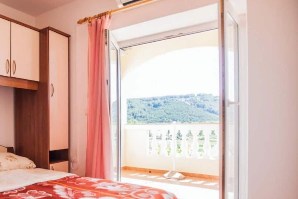 A bedroom with a bed, a wardrobe, a balcony with a view of greenery and hills.