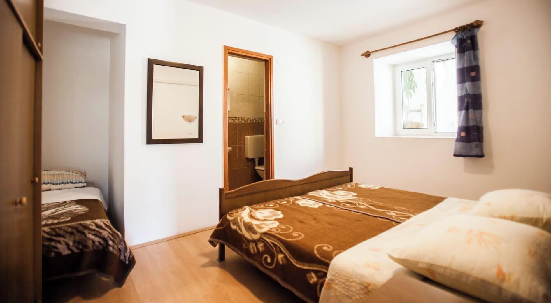Ein Schlafzimmer mit einem Bett, einem Nachttisch, einem Spiegel und einem Fenster mit Vorhängen.