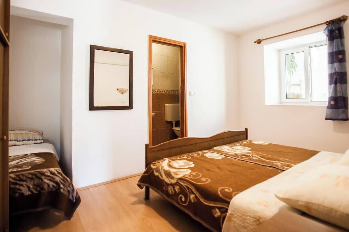 A bedroom with a bed, a bedside table, a mirror, and a window with curtains.