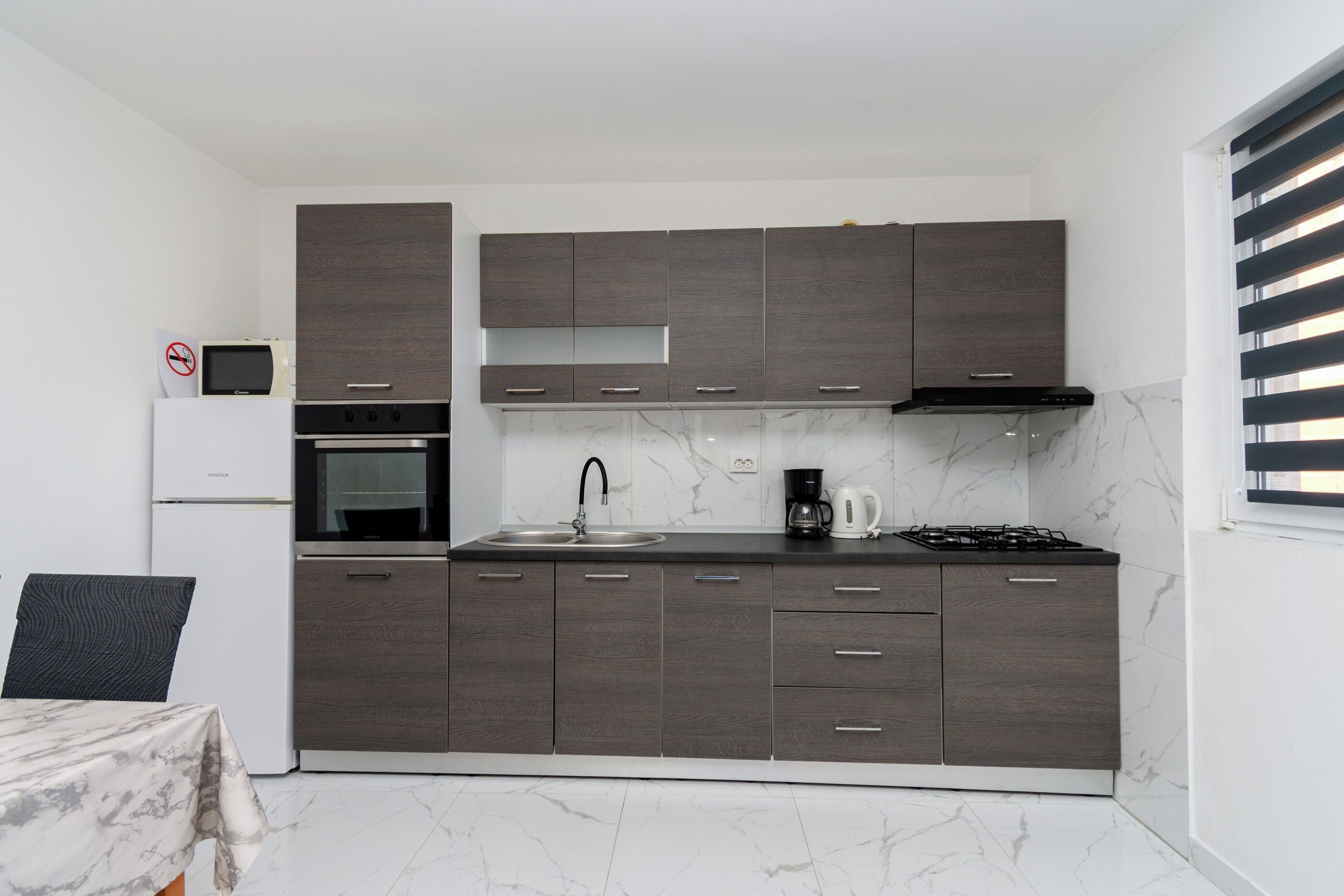 A modern kitchen with dark wood cabinets, a stainless steel sink, a stove, and a coffee maker.