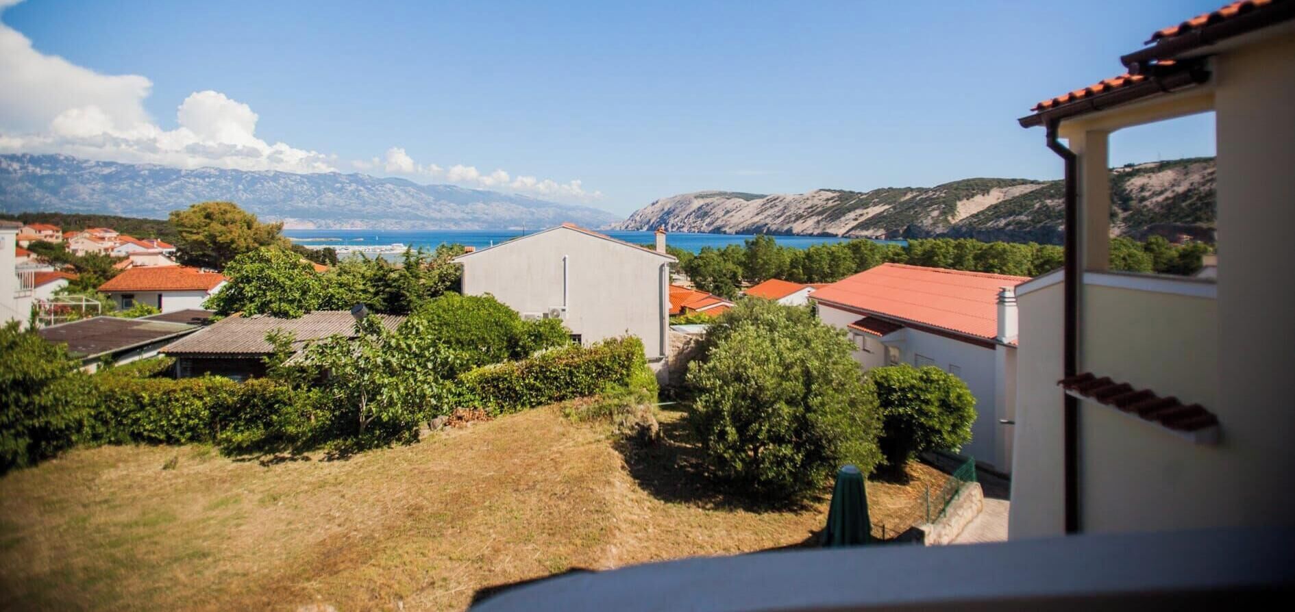 Ein Küstendorf mit Häusern, blauem Meer und Bergen im Hintergrund.