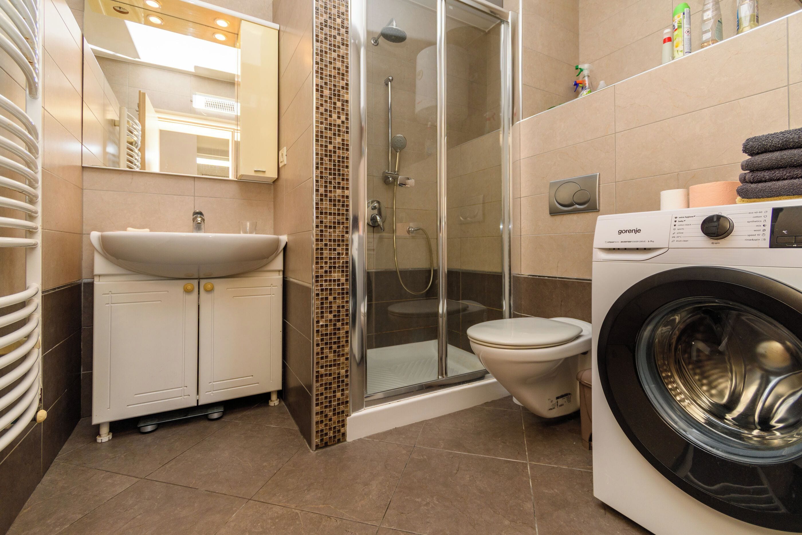 Une petite salle de bain d’hôtel comprenant un lavabo, des toilettes, une douche et un lave-linge.