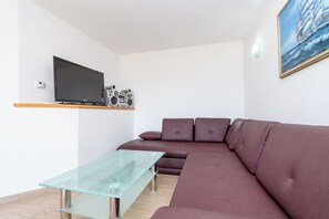 Uma sala de estar moderna com televisão de tela plana, uma mesa de centro de vidro, um sofá marrom e um quadro na parede.