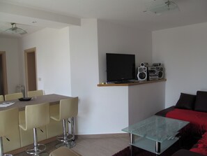 A modern living room with a glass-top coffee table, a flat-screen TV, and a sound system on a shelf. - Apartment Sea View (Opatija)