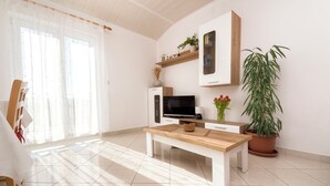 Ein modernes Wohnzimmer mit Couchtisch aus Holz, Flachbildfernseher, weißem Schrank und Topfpflanze.