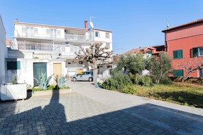 A residential street with a white two-story house, a red building, and a parked car. - Apartments Skriveni Dvori (Vodice)