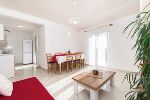 A bright living room with a dining area, a kitchen, and a large window. - Apartments Skriveni Dvori (Vodice)