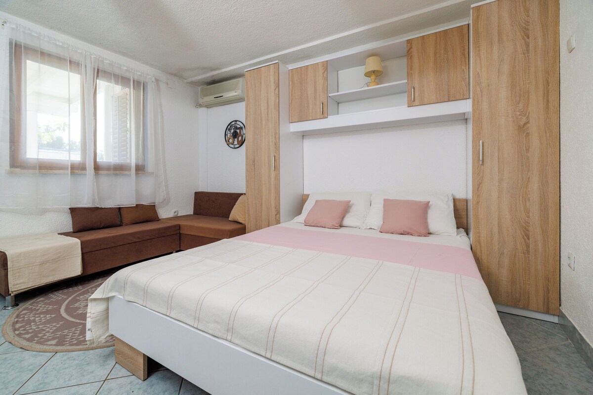Un dormitorio con cama, sofá, armarios de madera y ventana con cortinas translúcidas.