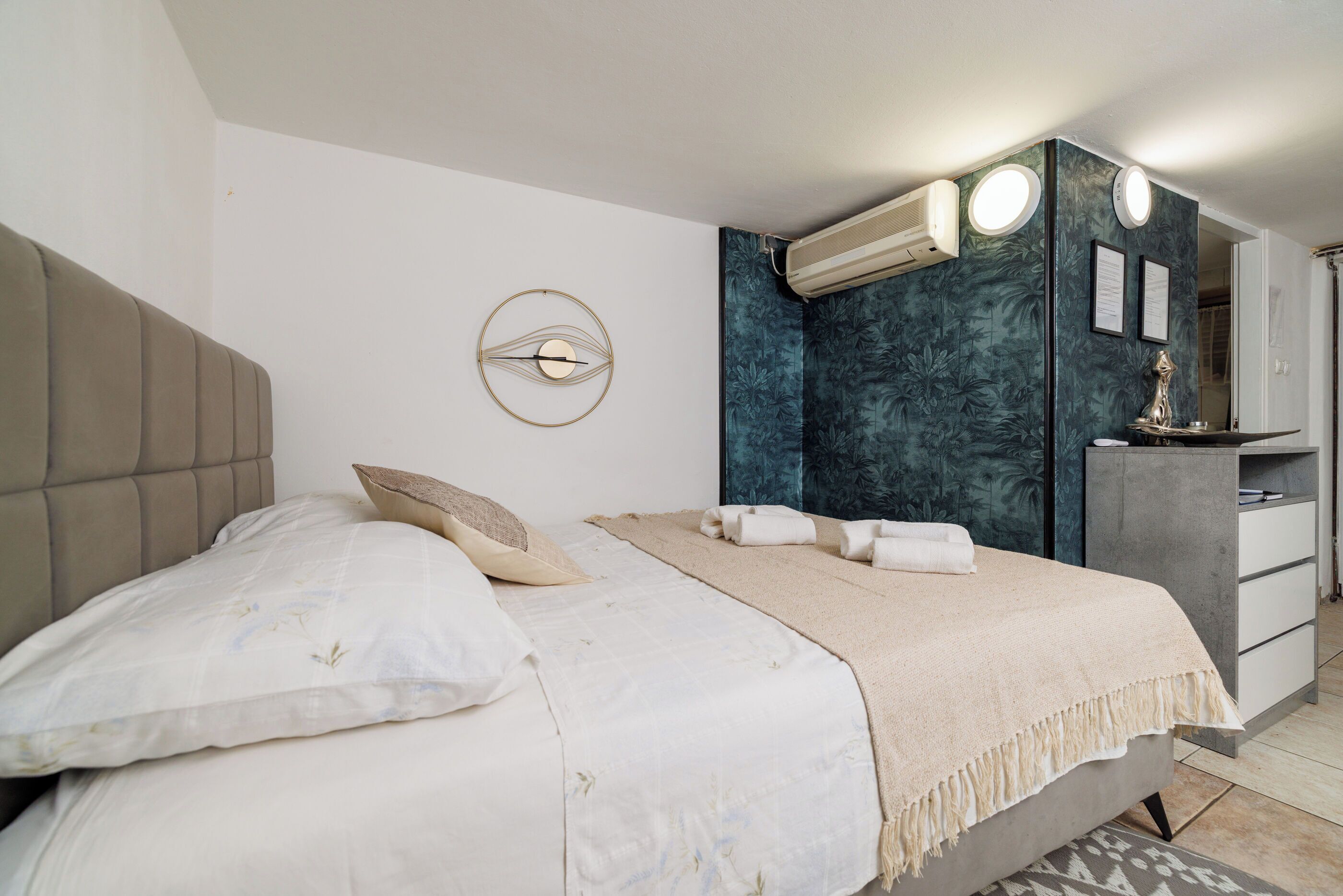 Ein Schlafzimmer mit einem Bett, einem Kopfteil, einer Wand-Klimaanlage, einem Nachttisch mit Lampe und einem Kleiderschrank.