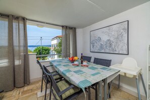 Ein Balkon mit Tisch, Stühlen, einem Hochstuhl und einem gerahmten Kunstwerk.