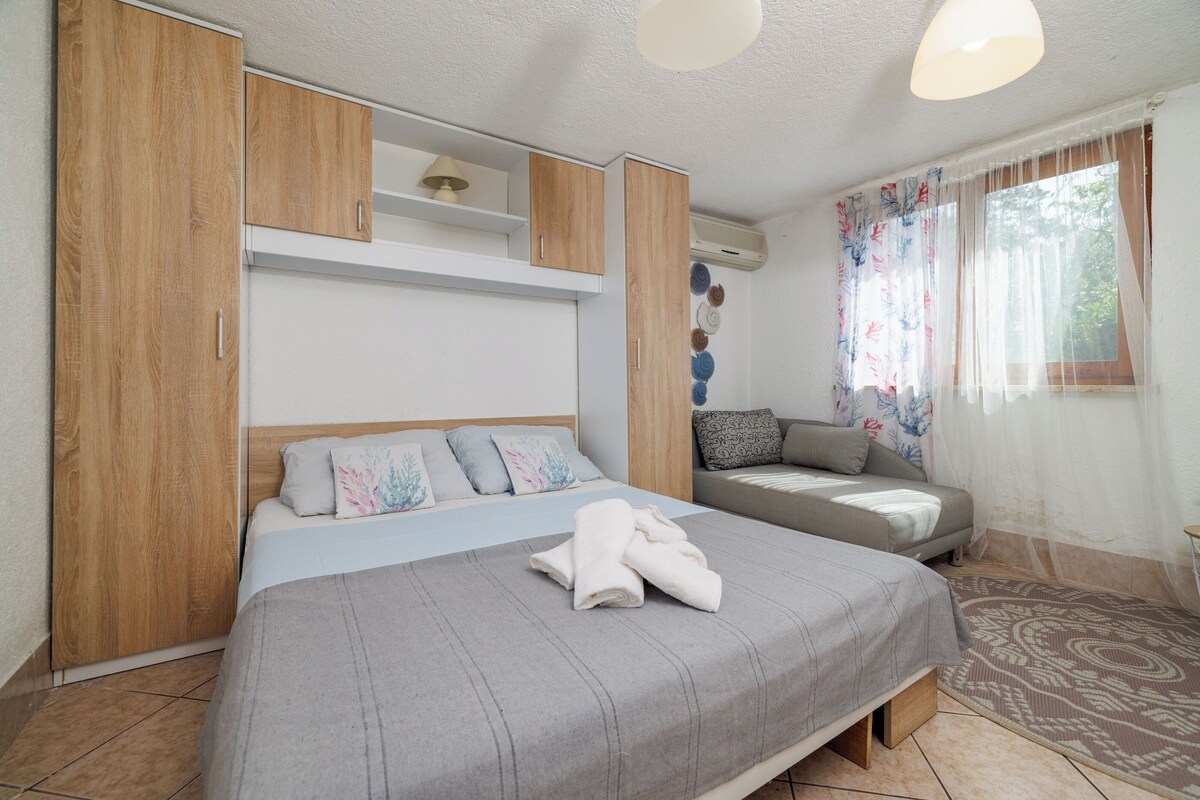 Un dormitorio con cama, sofá, armarios de madera, una lámpara de techo y una ventana con cortinas.