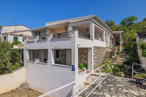 Ein zweistöckiges Gebäude mit einer Stein-Fassade, einem Balkon und einer Treppe, die zu einer zweiten Ebene führt.