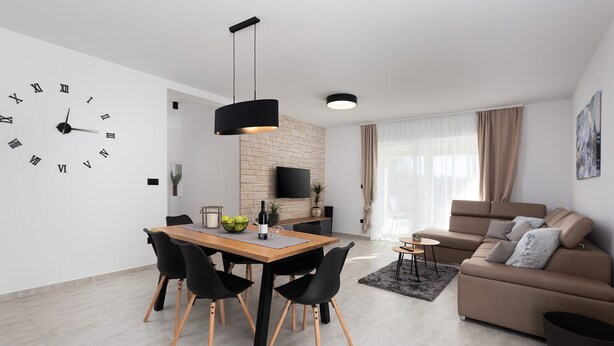 En moderne stue med en sofa, et spisebord med stole, et fjernsyn og et ur på væggen.