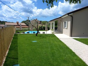 Ein Garten mit Schwimmbecken, Rasen und einem Gebäude mit überdachter Terrasse.
