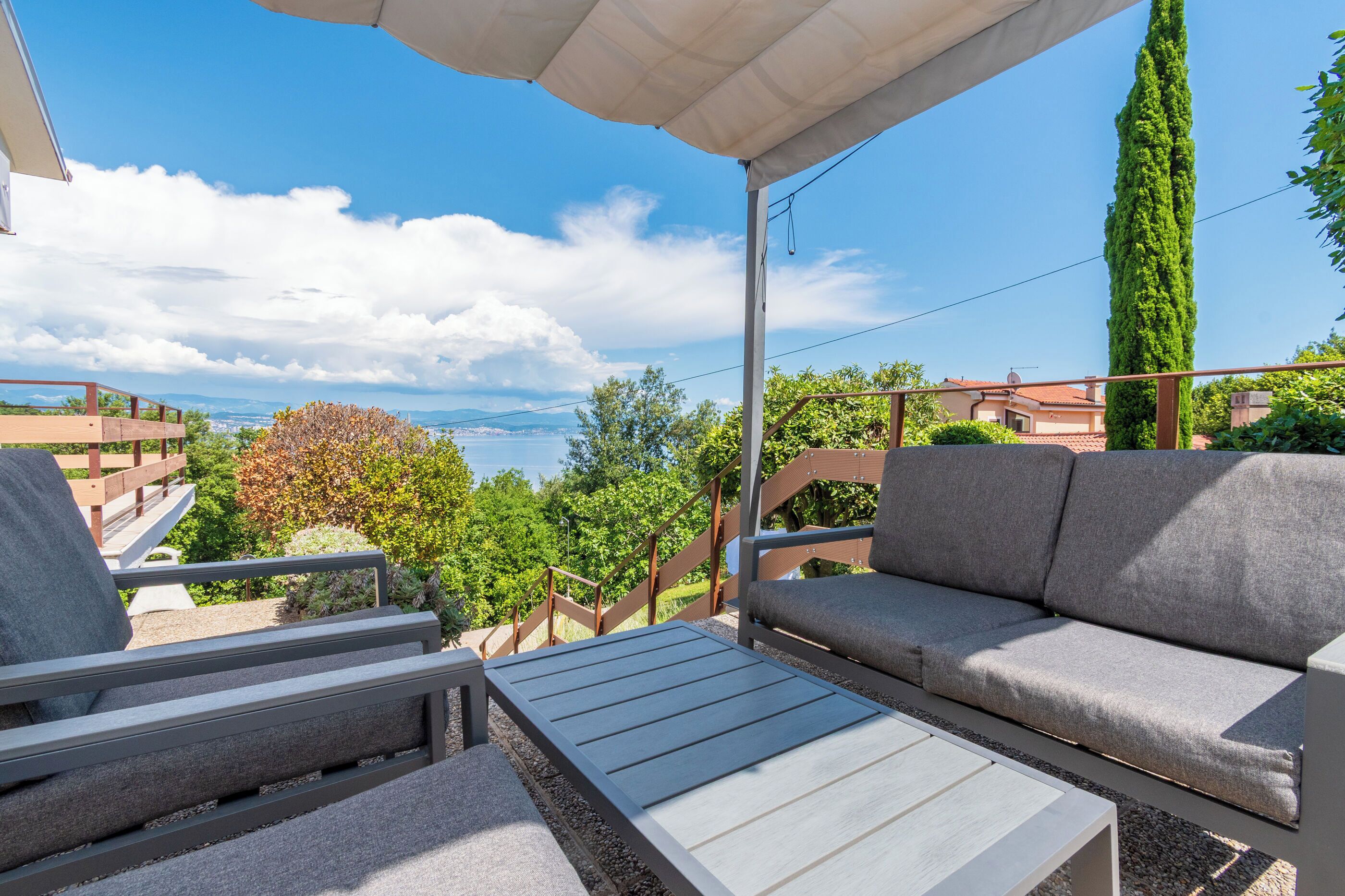 A balcony with a sofa, a table, and a view of the sea and mountains.