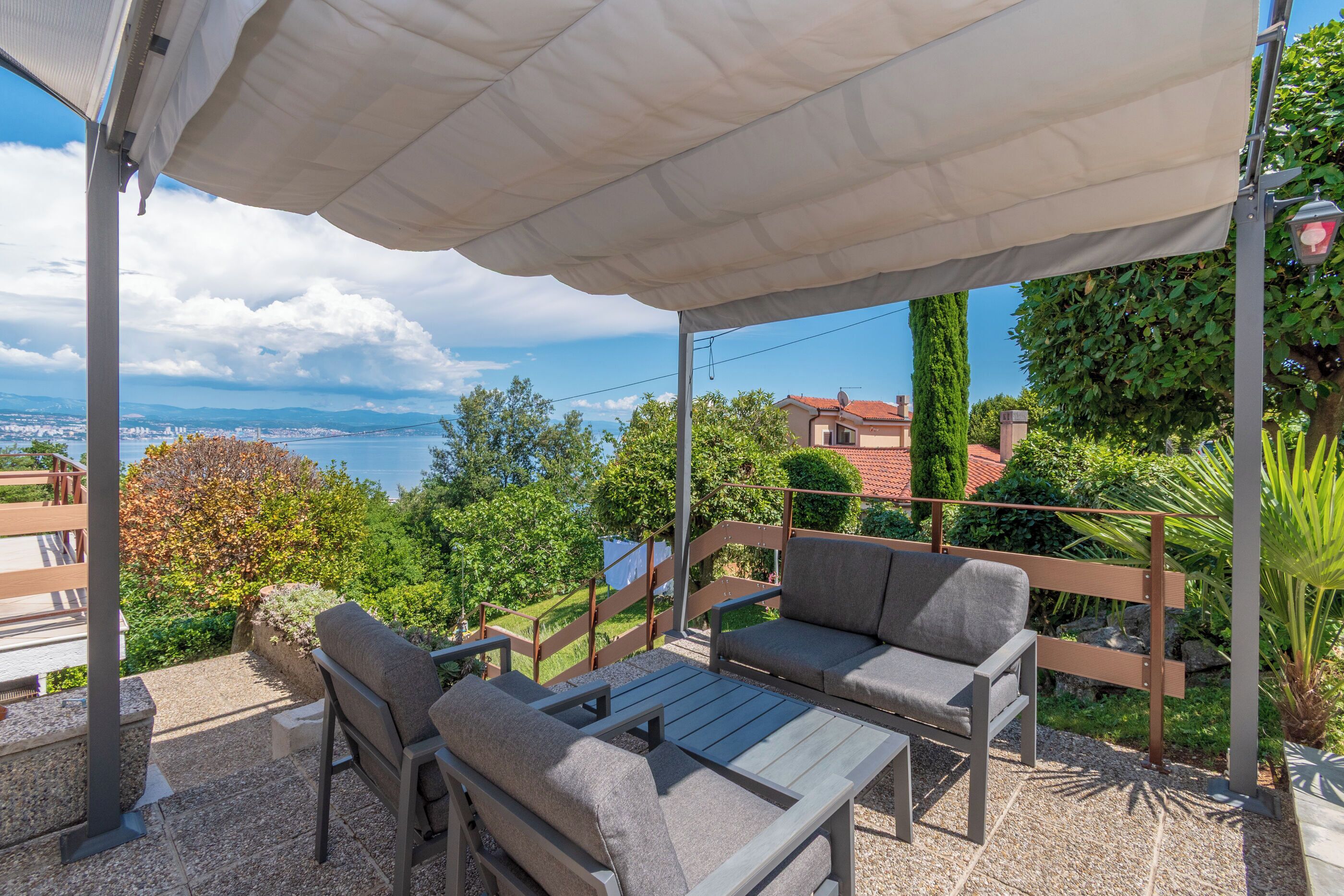 An outdoor patio with a table and chairs, a covered area, and a view of the sea and buildings.