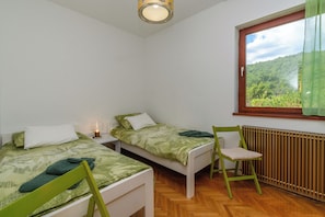 Ein Schlafzimmer mit zwei Einzelbetten, einem Sessel, einem Nachttisch und einem Fenster mit Blick ins Grüne.