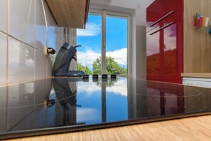 A kitchen with a reflective black countertop, a built-in stove, and a sliding glass door leading to an outdoor area. - Apartments Vida sea View (Opatija)