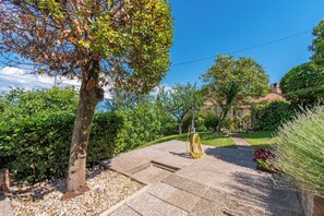 Ein gepflasterter Gartenweg mit einem Baum, einem Gartenschlauch und einem Gebäude im Hintergrund.