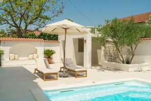 A pool area with lounge chairs and a canopy, a stone wall, and a white building with a tiled roof. - Apartments Bianca Vodice (Vodice)